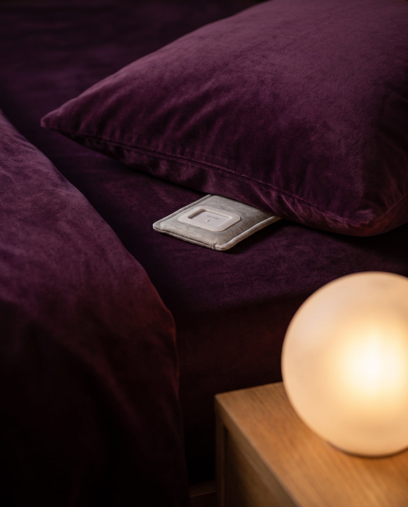The Drowsie speaker under a pillow at night, lit by a warm bedside lamp