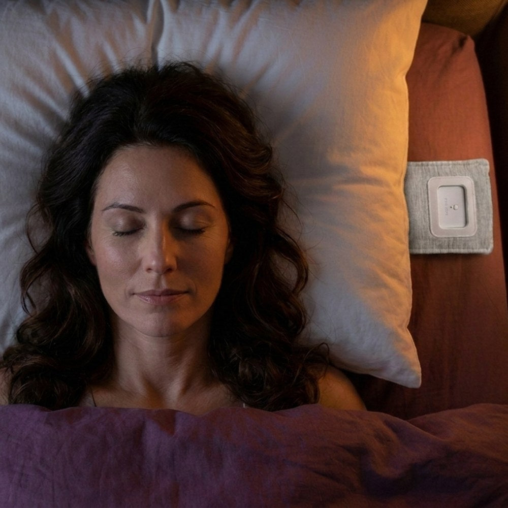 A woman asleep on her back, seen from above, the speaker under her pillow