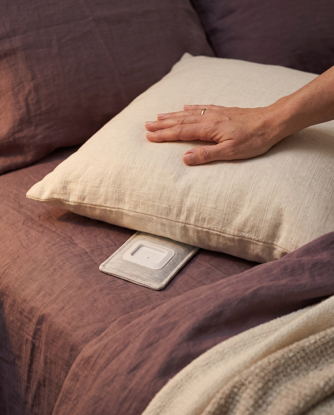 A hand smoothing a pillow, the Drowsie speaker tucked beneath it