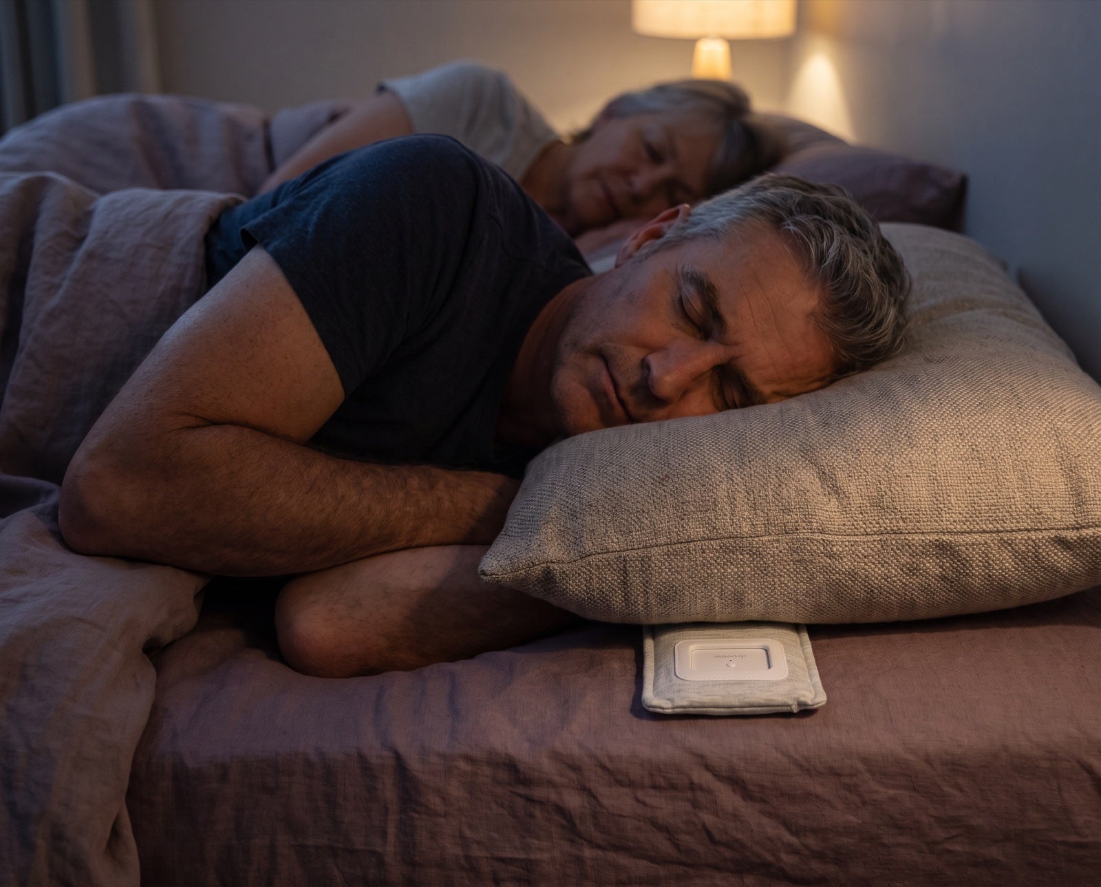 A man asleep on his side, the Drowsie speaker under the edge of his pillow